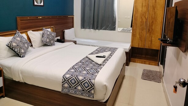 A hotel room with a large bed, a wooden wardrobe, a ceiling fan, and a window with curtains. - Yellow Sapphire Hotel Hitech City (Hyderabad)
