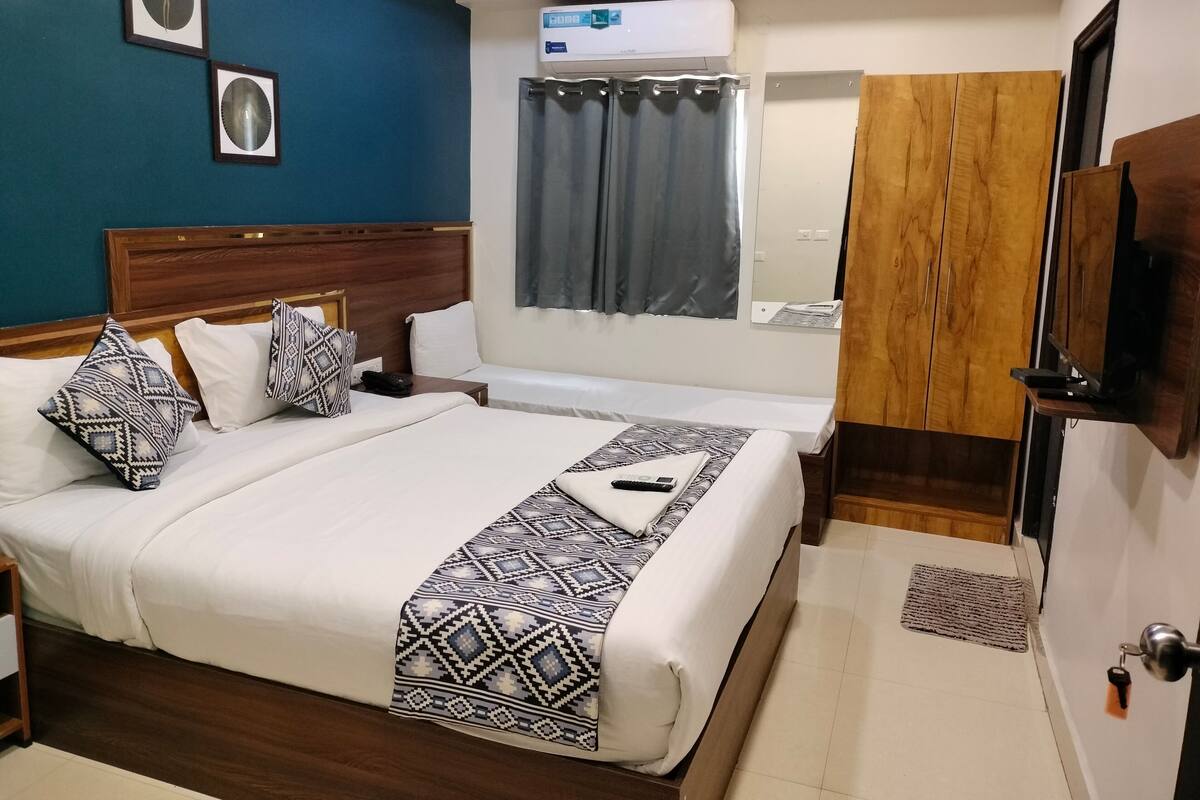 A hotel room with a large bed, a wooden wardrobe, a ceiling fan, and a window with curtains.