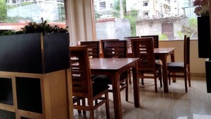 A dining area with wooden tables and chairs, a ceiling fan, and a view of buildings outside. - Yellow Sapphire Hotel Hitech City (Hyderabad)