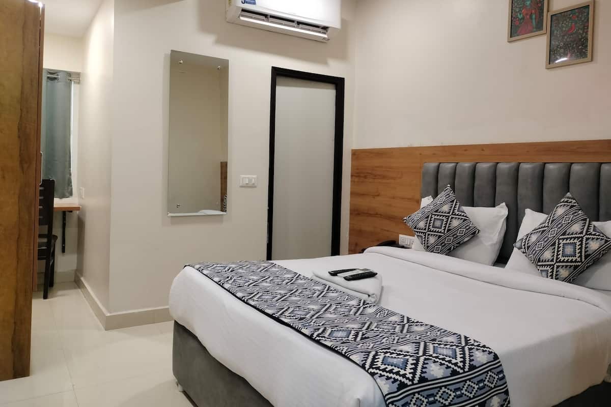 A hotel room with a bed, a bedside table, an air conditioning unit, a mirror, and two framed pictures on the wall.