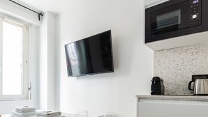 A modern hotel room with a bed, a round dining table with plates and cutlery, a television mounted on the wall, and a kitchenette with a microwave. - Cosy Apartment - 2P - Exhibitions Park (Paris)