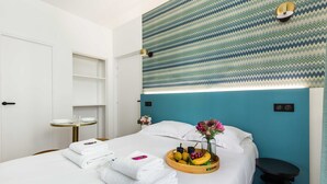 A hotel room with a bed, a bedside table with a tray of fruits and a vase of flowers, a small round table, and a wall with a zigzag pattern. - Cosy Apartment - 2P - Exhibitions Park (Paris)