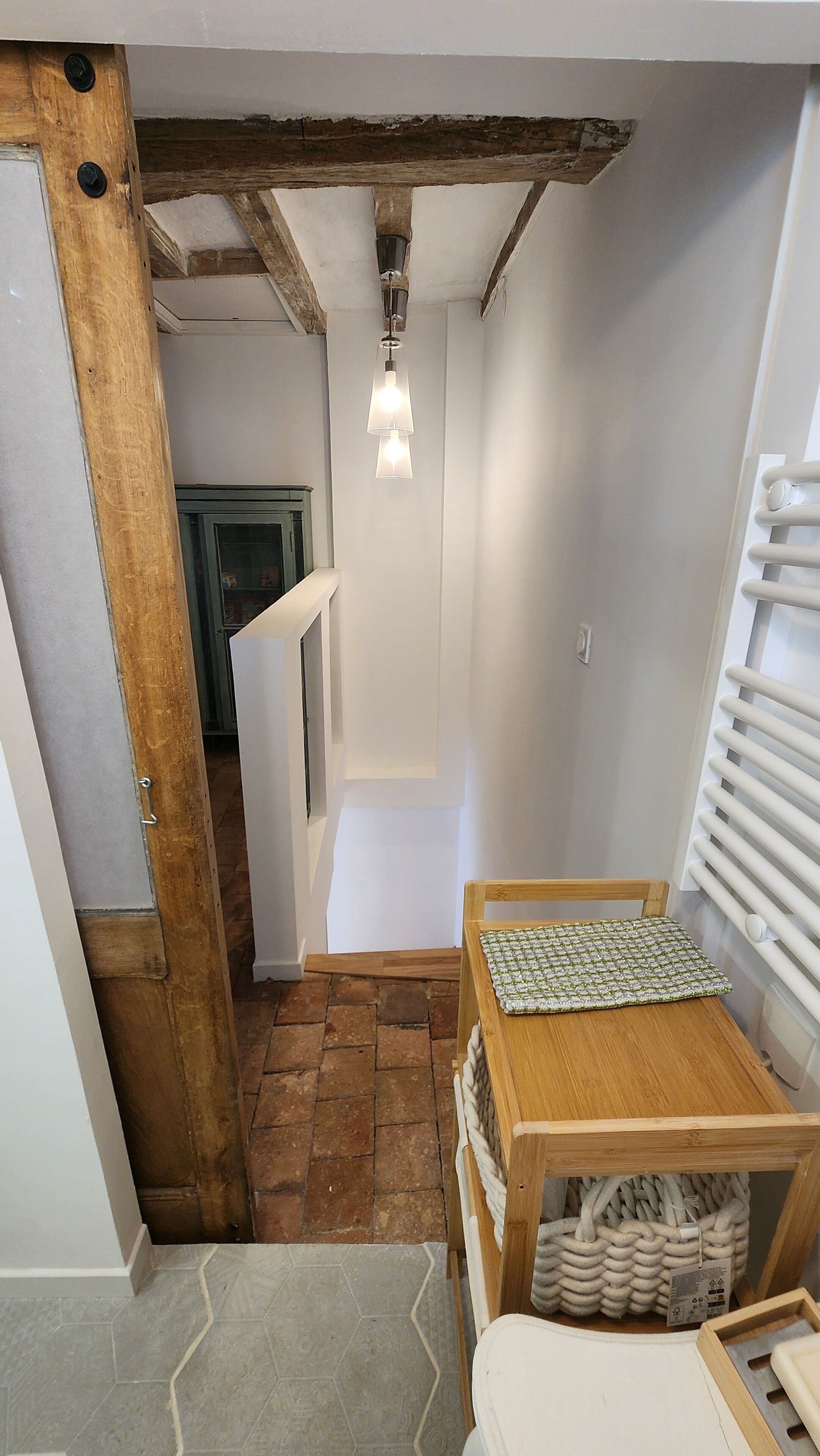 Um corredor estreito com uma porta de madeira, uma pequena mesa com toalha estampada e um lustre.