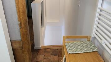 Um corredor estreito com uma porta de madeira, uma pequena mesa com toalha estampada e um lustre.
