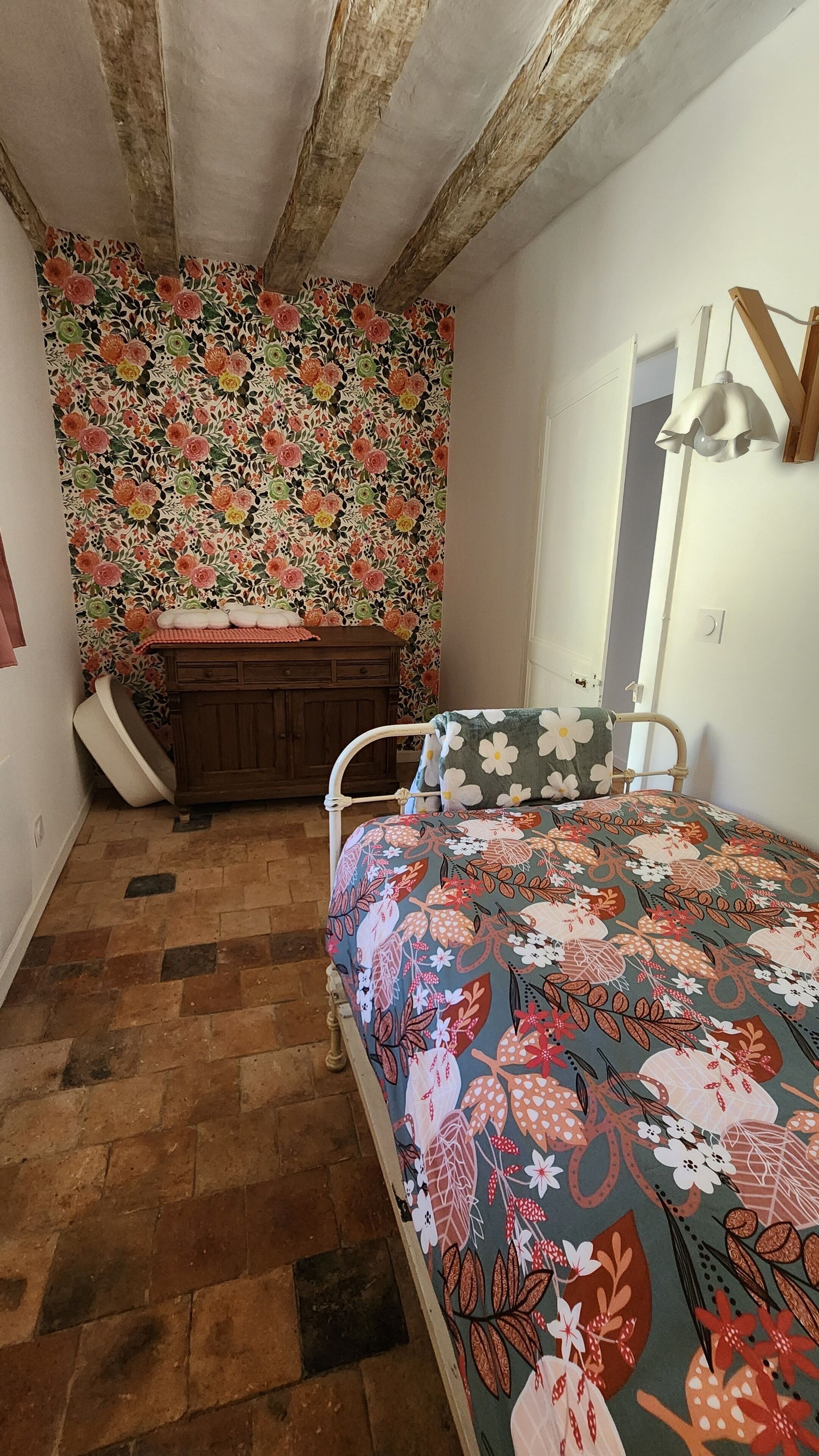 Ein Schlafzimmer mit einem blumigem Bettüberwurf, einem Holzschrank und einer schrägen Decke.