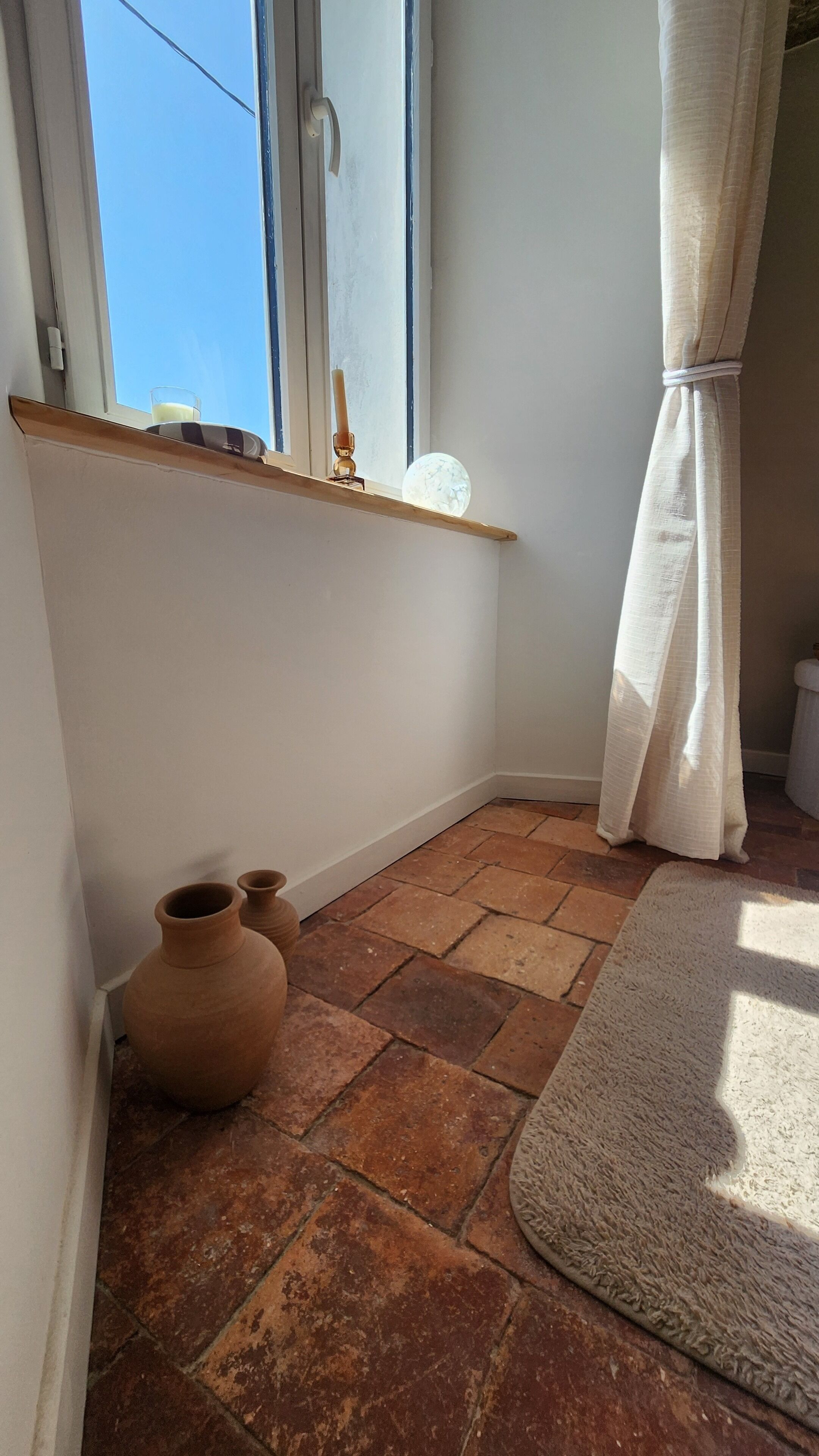 Ein Zimmer mit Fenster, einem Regal mit einem Glas Milch, einer Kerze und zwei Tongefäßen auf dem Boden.