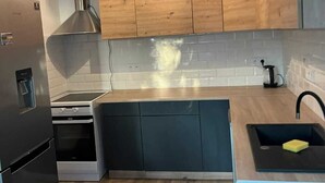 Eine moderne Küche mit Holzausstattung, einem eingebauten Ofen, einem Edelstahlkühlschrank und einer schwarzen Spüle.