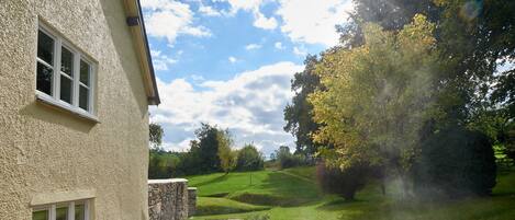 A hot tub in a backyard with a stone wall, a window, and a view of a golf course.