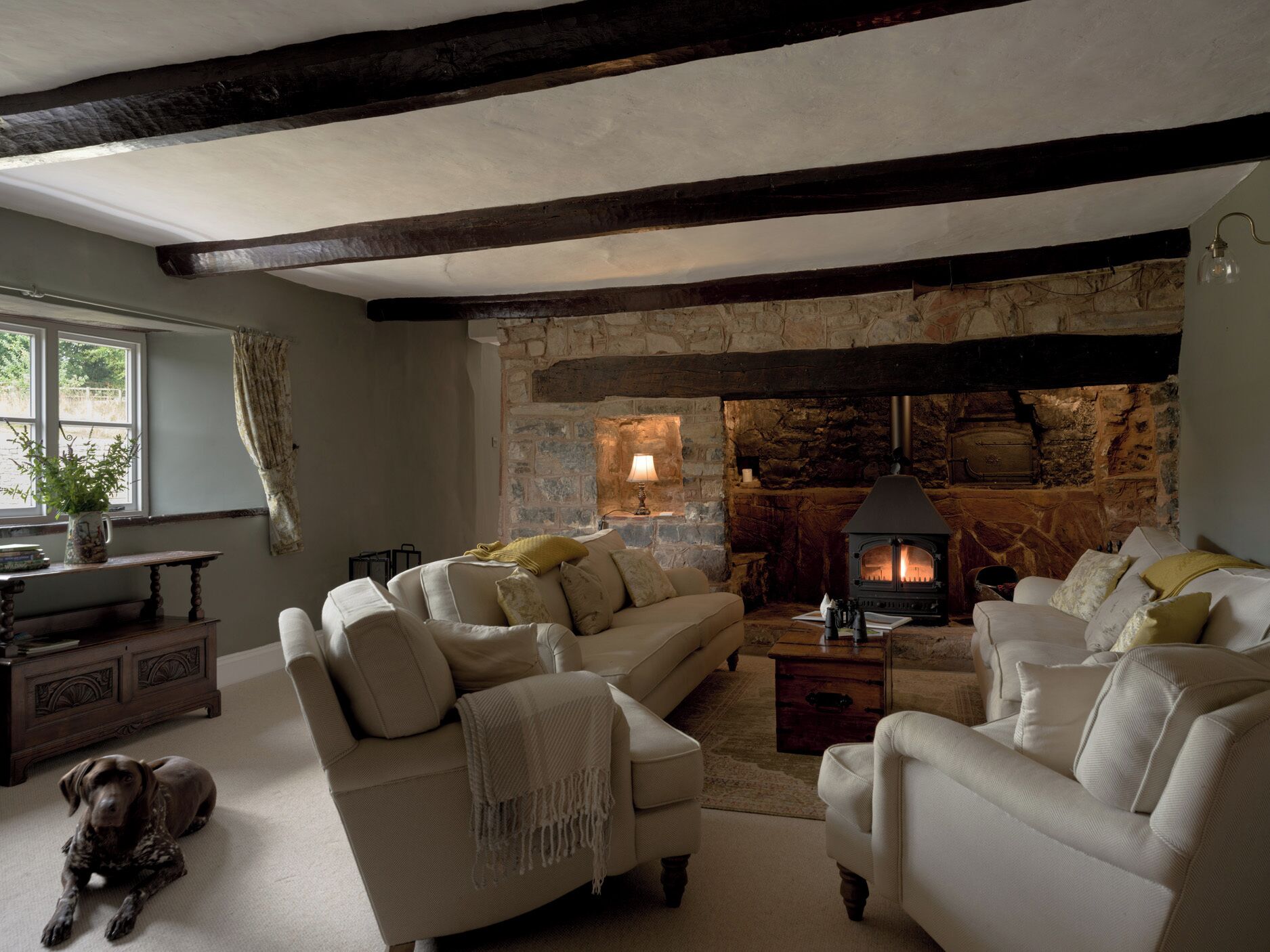 A cozy living room with a stone fireplace, two sofas, a dog, and a rustic wooden table.