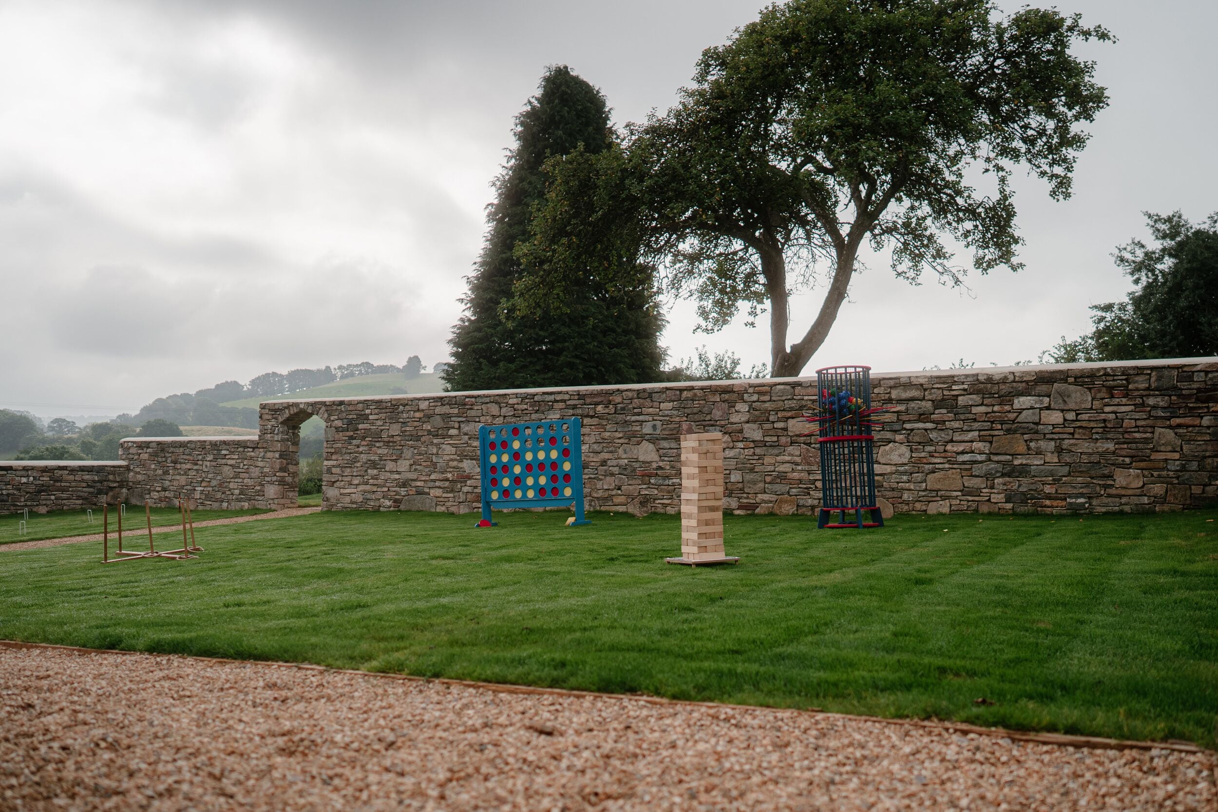 Un mur de pierres avec une clôture en bois, une zone herbeuse et un arbre.
