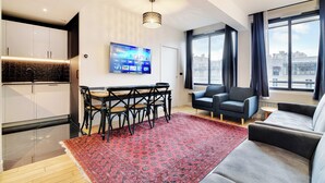 A modern living room with a sofa, a TV mounted on the wall, and a large window with curtains. - Modern Apartment - 2br/8p - Near Opera Garnier (Paris)