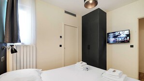 A hotel room with a bed, a TV mounted on the wall, a door, and a window with curtains. - Modern Apartment - 2br/8p - Near Opera Garnier (Paris)