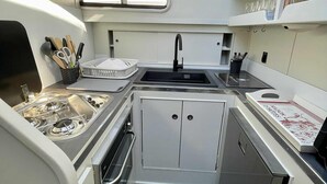 A compact galley kitchen with a sink, stove, and storage cabinets, featuring skylights and a small window. - IRIS BATEAU DOUILLET (Nevers)