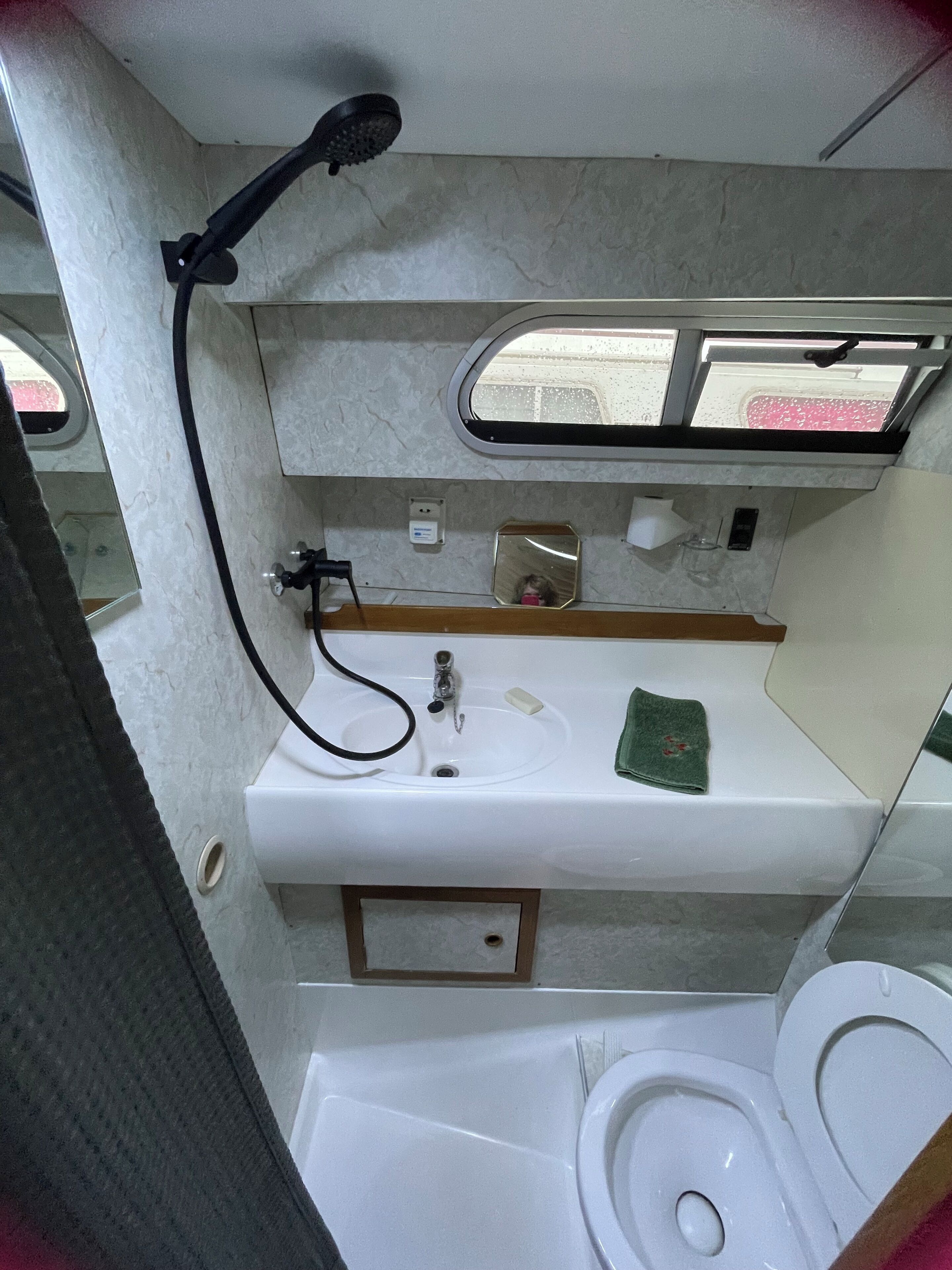 Un baño pequeño con un lavamanos blanco, un espejo, un cabezal de ducha manual y un inodoro.