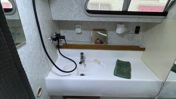Un baño pequeño con un lavamanos blanco, un espejo, un cabezal de ducha manual y un inodoro.