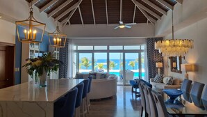 A spacious living area with a high ceiling, a large window overlooking a pool, and a bar area with stools.