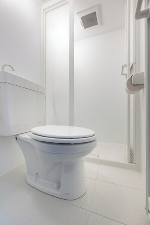 A white toilet with a tank, a shower area with a glass door, and a white tiled floor. - Sleep Inn Gotanda (Tokyo)