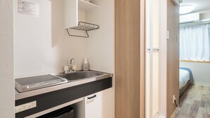 A compact kitchen with a sink, a small countertop, and a microwave. There is a shelf above the sink and a cabinet below it. - Sleep Inn Gotanda (Tokyo)