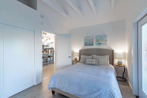 A bedroom with a bed, bedside tables, a nightstand, a chair, and a dining area visible through an open door. - Coastal Charm - Oceanview Stay in Pacifica Near SF (Pacifica)