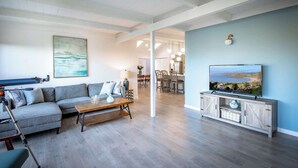 A living room with a sectional sofa, a coffee table, a TV on a cabinet, and a dining area in the background. - Coastal Charm - Oceanview Stay in Pacifica Near SF (Pacifica)
