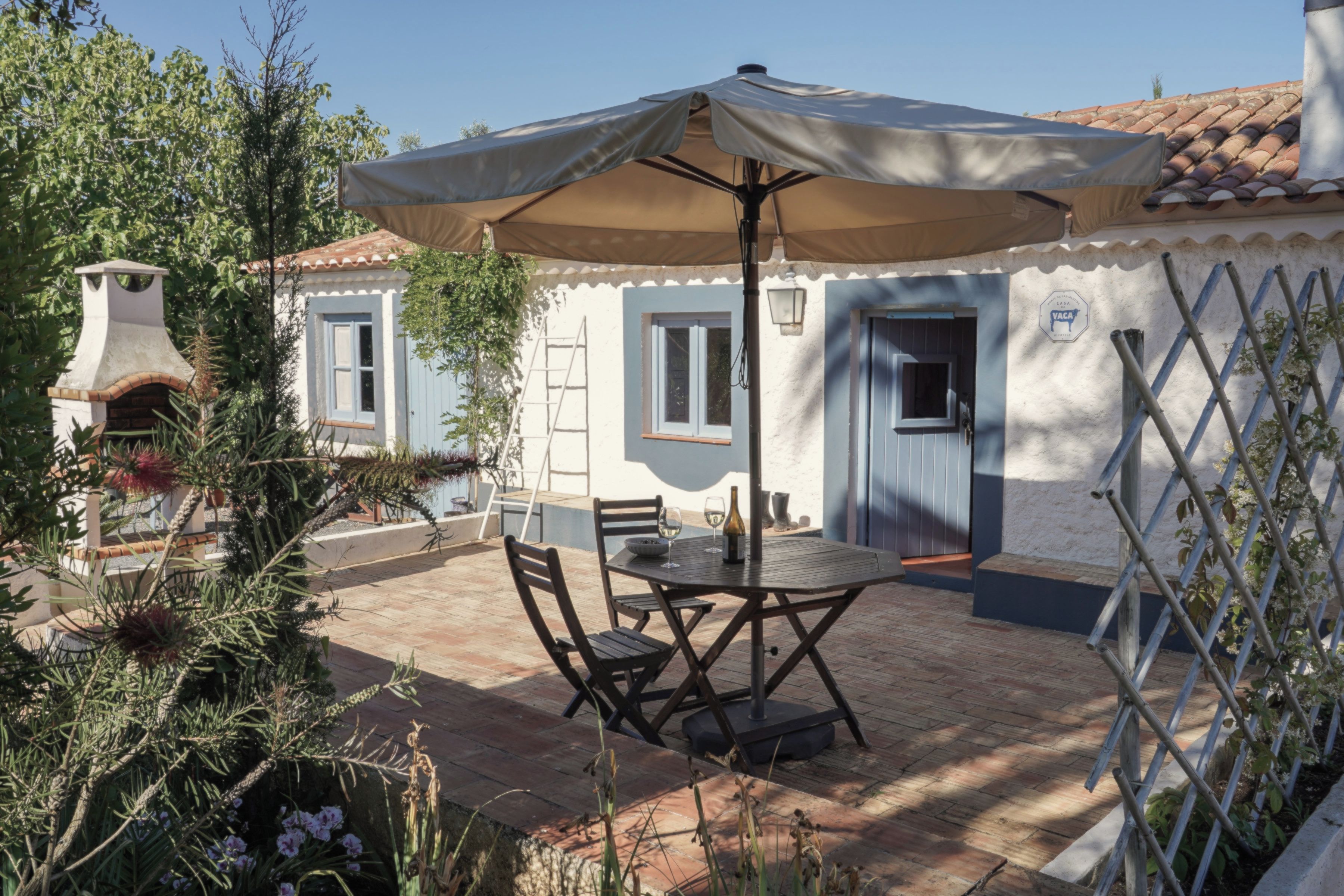 Une terrasse extérieure avec une table et des chaises, un barbecue et un espace abrité avec un parasol.