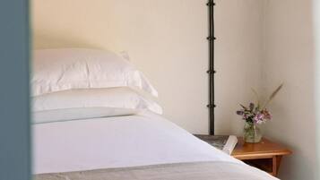 Una cama bien hecha con sábanas blancas, una mesita de noche con un florero y una lámpara alta de color negro.