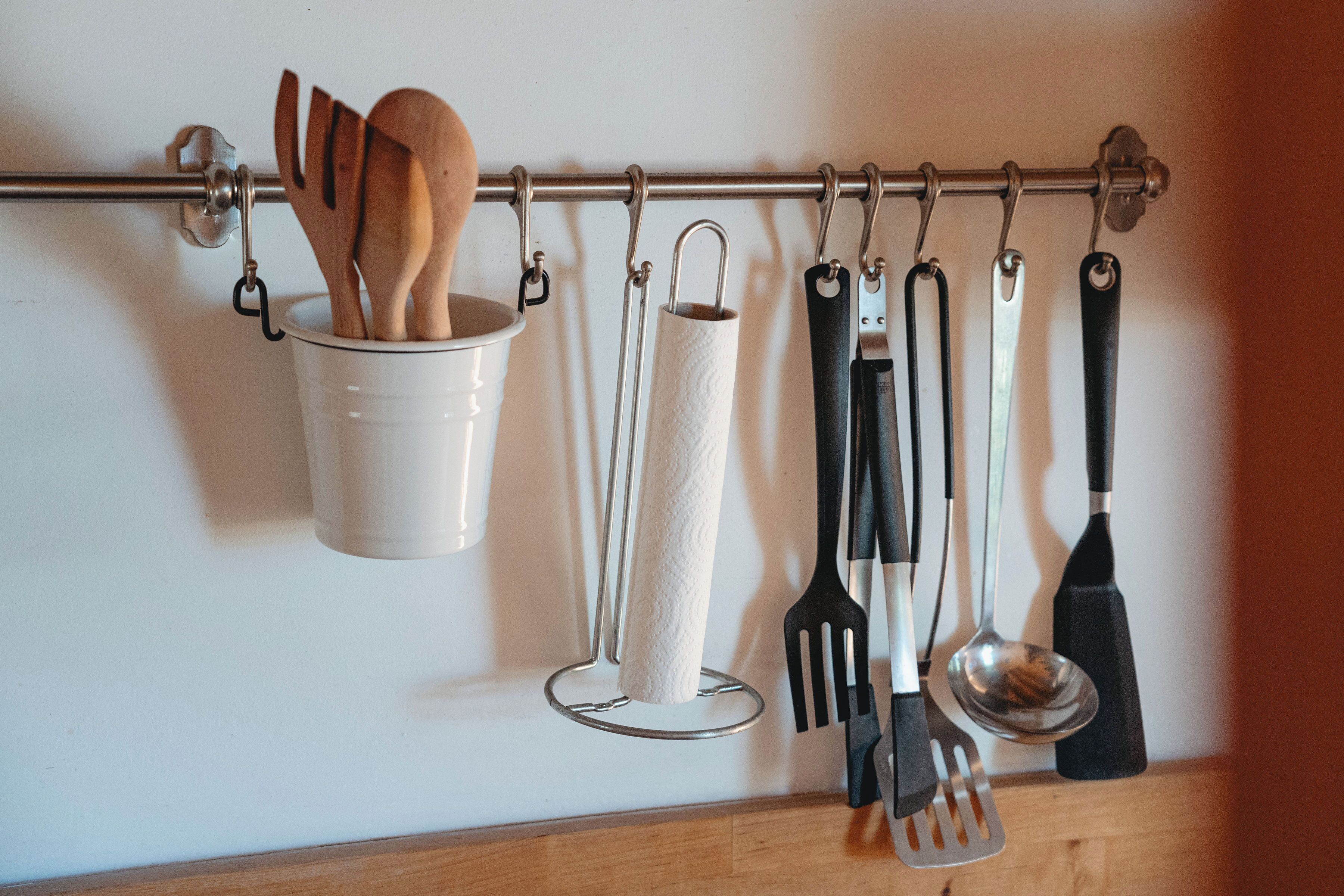 Un escurridor de utensilios de cocina con cucharas de madera, un dispensador de toallas de papel y diferentes herramientas de cocina.