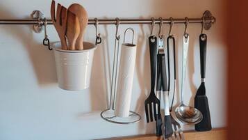 Un escurridor de utensilios de cocina con cucharas de madera, un dispensador de toallas de papel y diferentes herramientas de cocina.