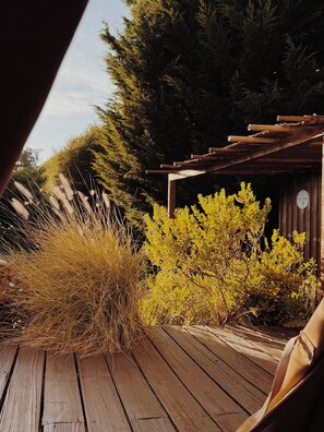 Eine Holzterrasse mit einer rustikalen Holzkonstruktion, umgeben von verschiedenen Sträuchern und Gräsern.