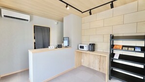 A reception area with a wooden desk, a computer, a microwave, and a bookshelf. - NikkaHotel togo (Togo)