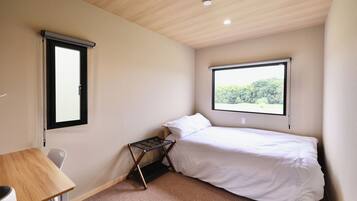 Un dormitorio con una cama individual, un escritorio y una ventana con vistas a árboles.