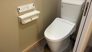 A white toilet with a control panel on the wall, a toilet paper holder, and a tiled floor. - NikkaHotel togo (Togo)