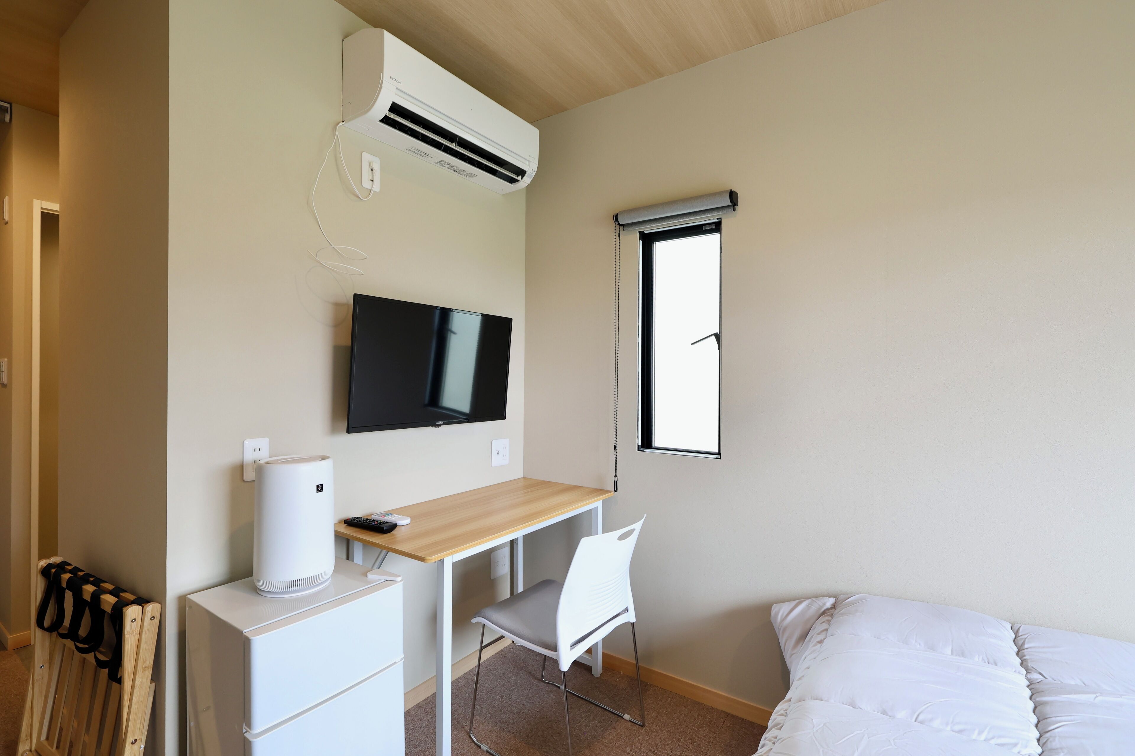 A bedroom with a bed, a desk with a chair, a TV, an air conditioner, and a window.