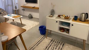 A compact living space with a sofa, a small dining table, a TV mounted on the wall, a kitchen area with a microwave, a kettle, and a small cabinet. - Sunny Haven 1BR Apartment: A Luxurious Retreat near Cairo Airport (Cairo Governorate)