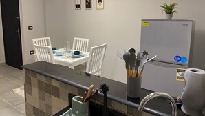 A modern kitchen with a dining area, featuring a refrigerator, a sink, and a countertop with utensils. - Sunny Haven 1BR Apartment: A Luxurious Retreat near Cairo Airport (Cairo Governorate)