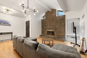 Una sala de estar moderna con chimenea de piedra, sofás grises, una mesa de centro redonda y una lámpara en el techo.