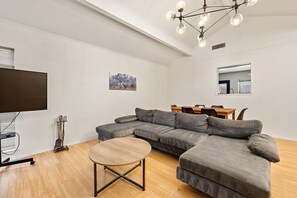 Una sala de estar moderna con un sofá modular, una mesa de centro redonda de madera y un comedor con mesa y sillas de madera.
