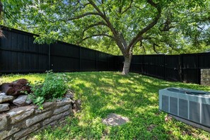 A backyard with a tree, a stone wall, and an air conditioning unit.