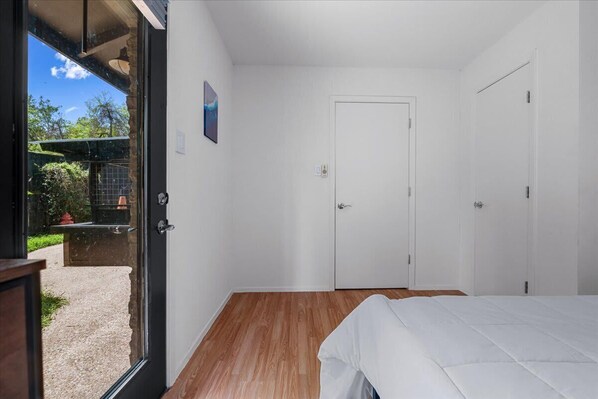 Un dormitorio con piso de madera, una cama blanca y una puerta que da a un espacio exterior.