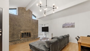 A modern living room with a stone wall, a gray sofa, a wooden dining table, and a chandelier. - Elevated Austin Escape | 4BR + Pool (Austin)