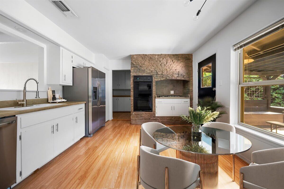 A modern kitchen with white cabinets, a stone accent wall, and a dining area with a glass table and chairs.