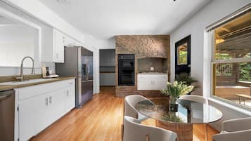 A modern kitchen with white cabinets, a stone accent wall, and a dining area with a glass table and chairs.