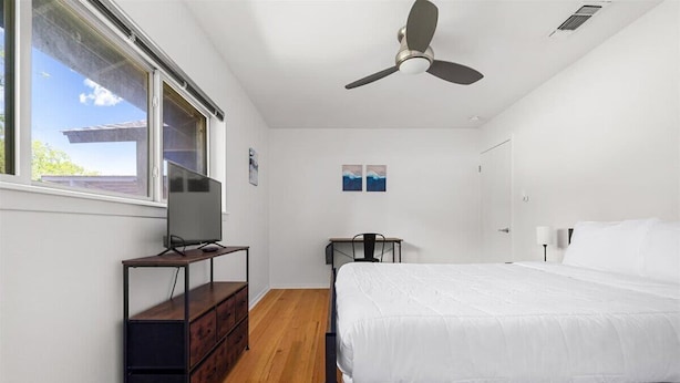 A bedroom with a bed, a desk, a chair, a TV on a stand, and a ceiling fan. - Elevated Austin Escape | 4BR + Pool (Austin)