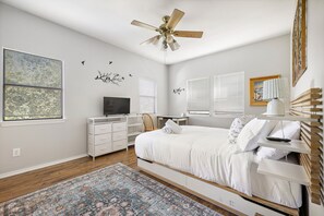 Une chambre à coucher comprenant un lit, un bureau, une chaise, un téléviseur et un ventilateur de plafond.