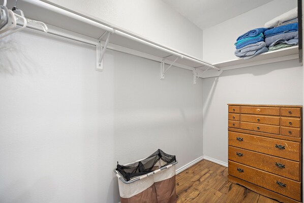 A closet with a white wall, a wooden floor, and a wooden dresser with multiple drawers.