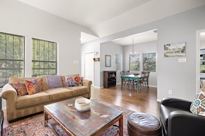 A spacious living room with a beige sofa, a coffee table, and a dining area with a green table and chairs.