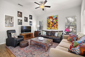 A living room with a flat-screen TV, a ceiling fan, a coffee table, a sofa, and a patterned rug. - Classic South 5th Getaway by Barclé (Austin)