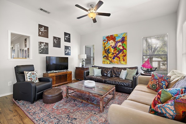 A living room with a flat-screen TV, a ceiling fan, a coffee table, a sofa, and a patterned rug.