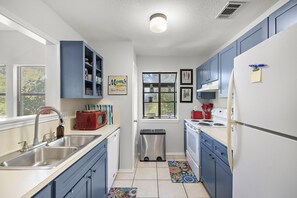 Una cocina compacta con armarios azules, un lavamanos de acero inoxidable, un refrigerador y una ventana con persianas.