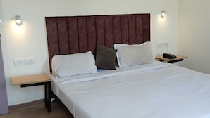A bedroom with a large bed, a wooden nightstand, a bedside table, and a wall-mounted lamp.